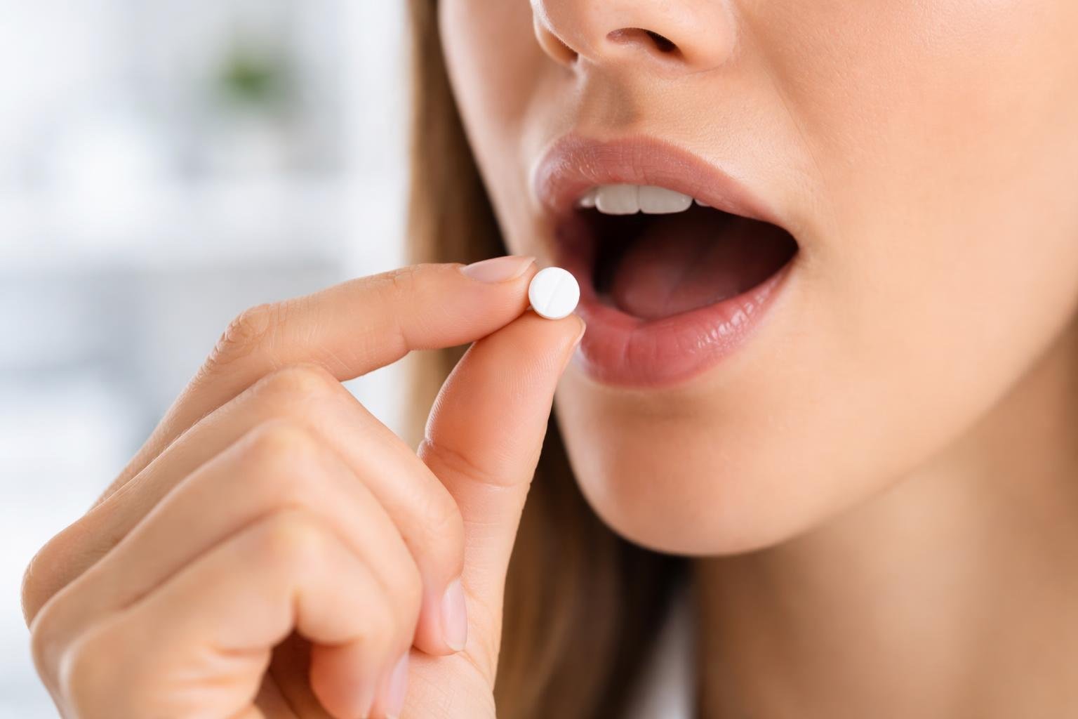 Pessoa segurando um comprimido sublingual próximo à boca aberta, pronta para colocar o medicamento sob a língua.